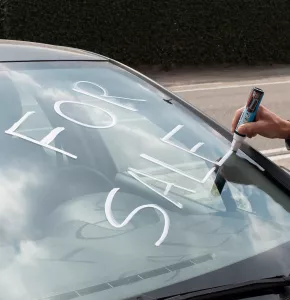 Persona que escribe con un rotulador de ventana borrable blanco en la ventana de un automóvil