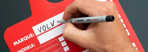 Jemand schreibt mit einem schwarzen Marker auf eine rote Verkaufskarte