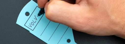 Jemand schreibt mit einem schwarzen Permanentmarker auf einen blauen Schlüsselanhänger mit Schlaufe